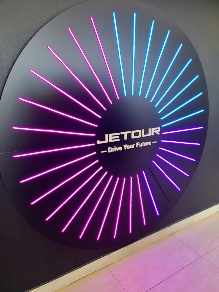 Logo de Jetour iluminado con luces LED en colores rosa y azul sobre fondo oscuro